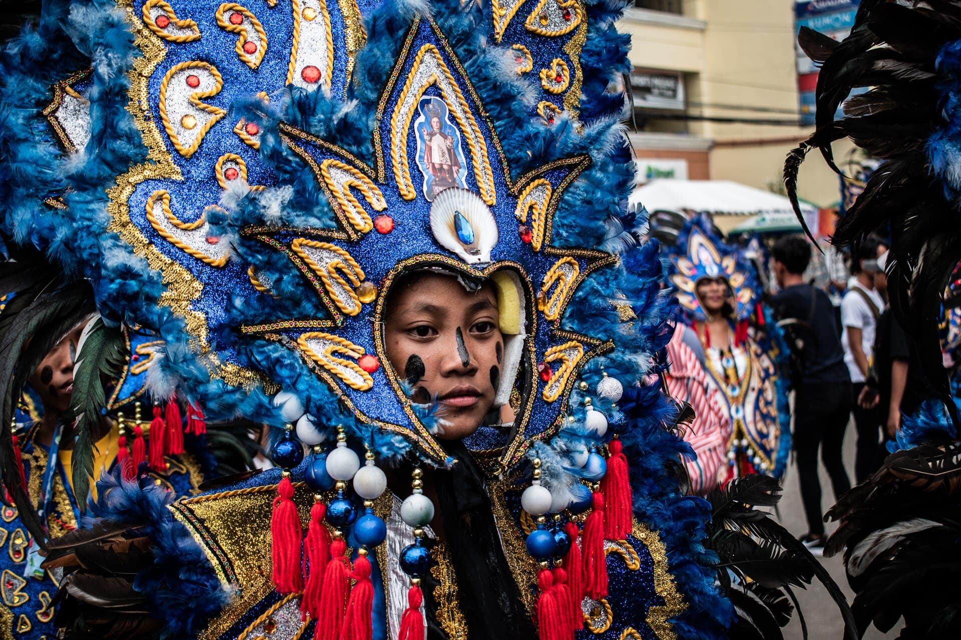 Close portrait of a participant with black body paint and a large peacock-style headdress at the Kalibo Ati-Atihan