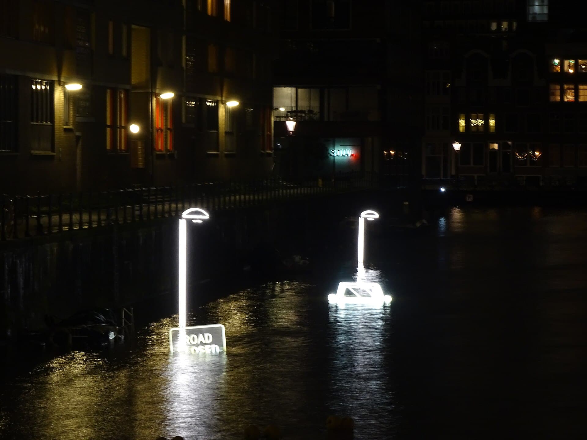 An open electric boat carrying passengers under a canal-side artwork