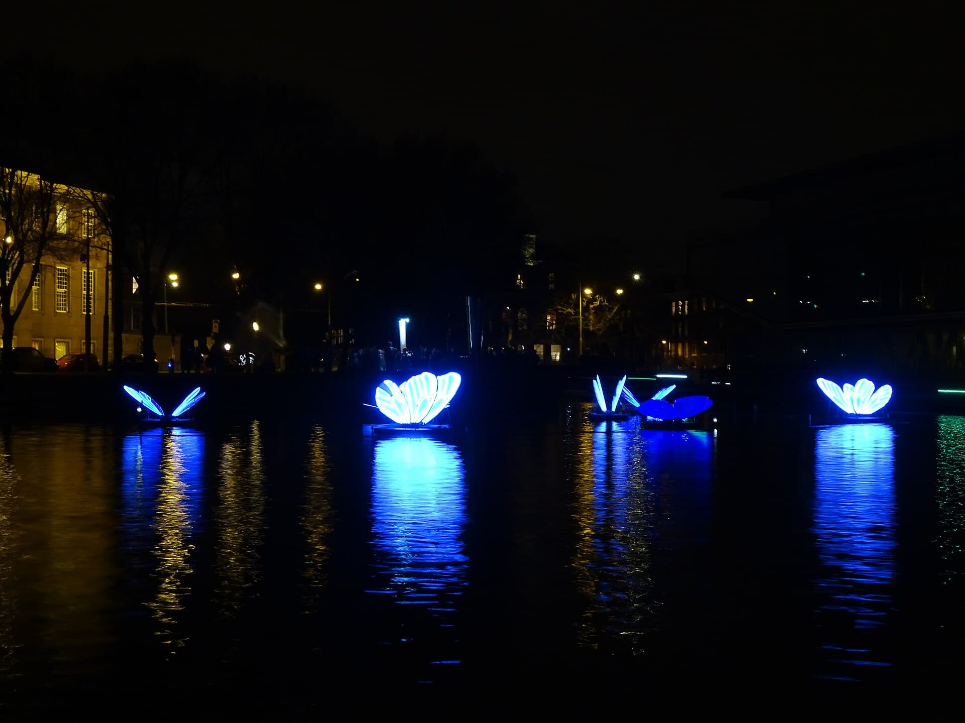 Visitors in winter coats walking along a canal quay past a light installation