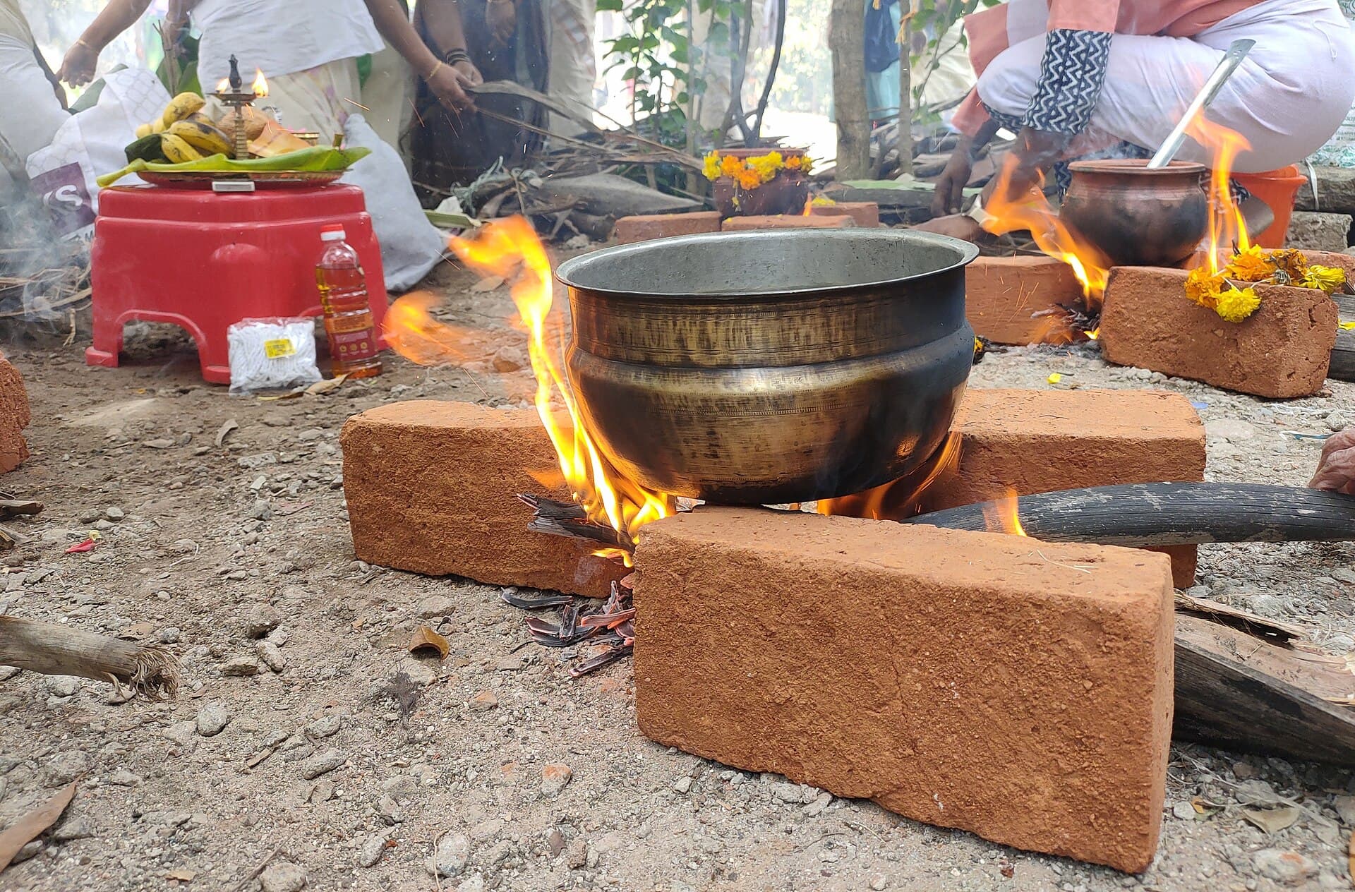 Pongala payasam boiling over in an earthen pot on a brick hearth