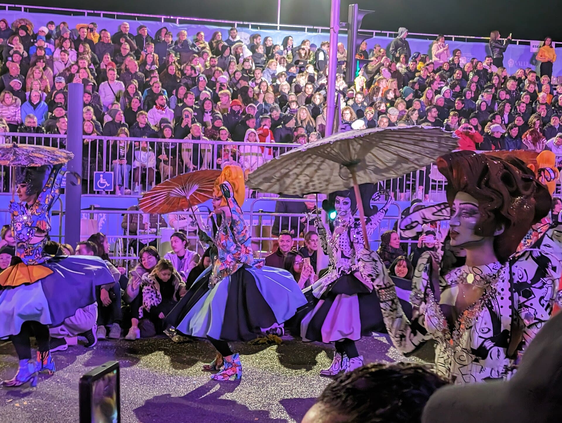 Illuminated carnival float passing Place Masséna in Nice at night with crowds in the grandstands