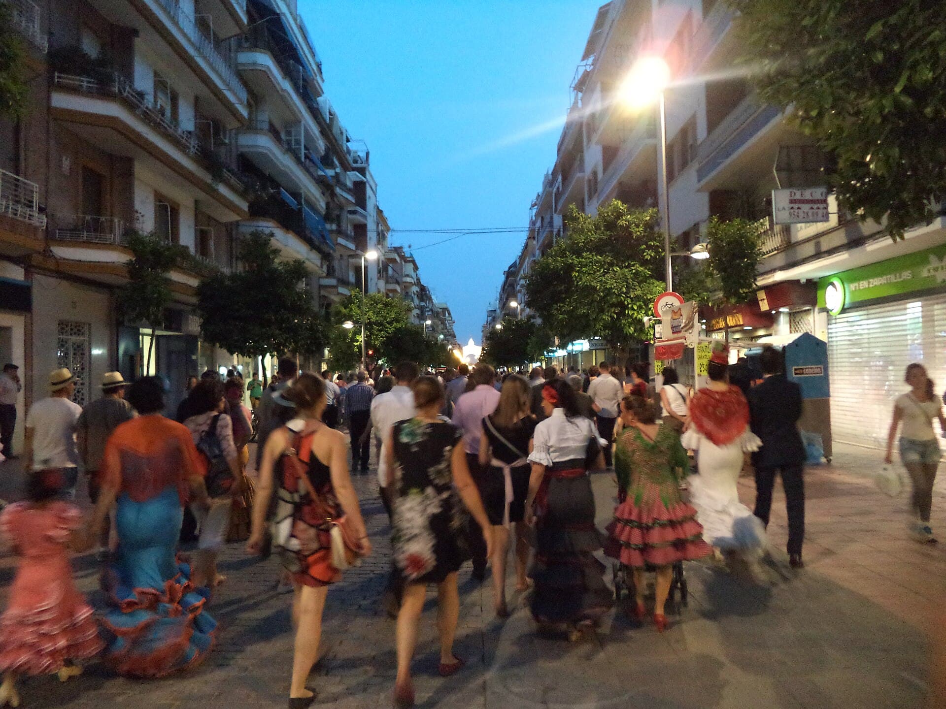 The lit portada of the Feria de Abril de Sevilla at night, wide shot from Calle Asunción