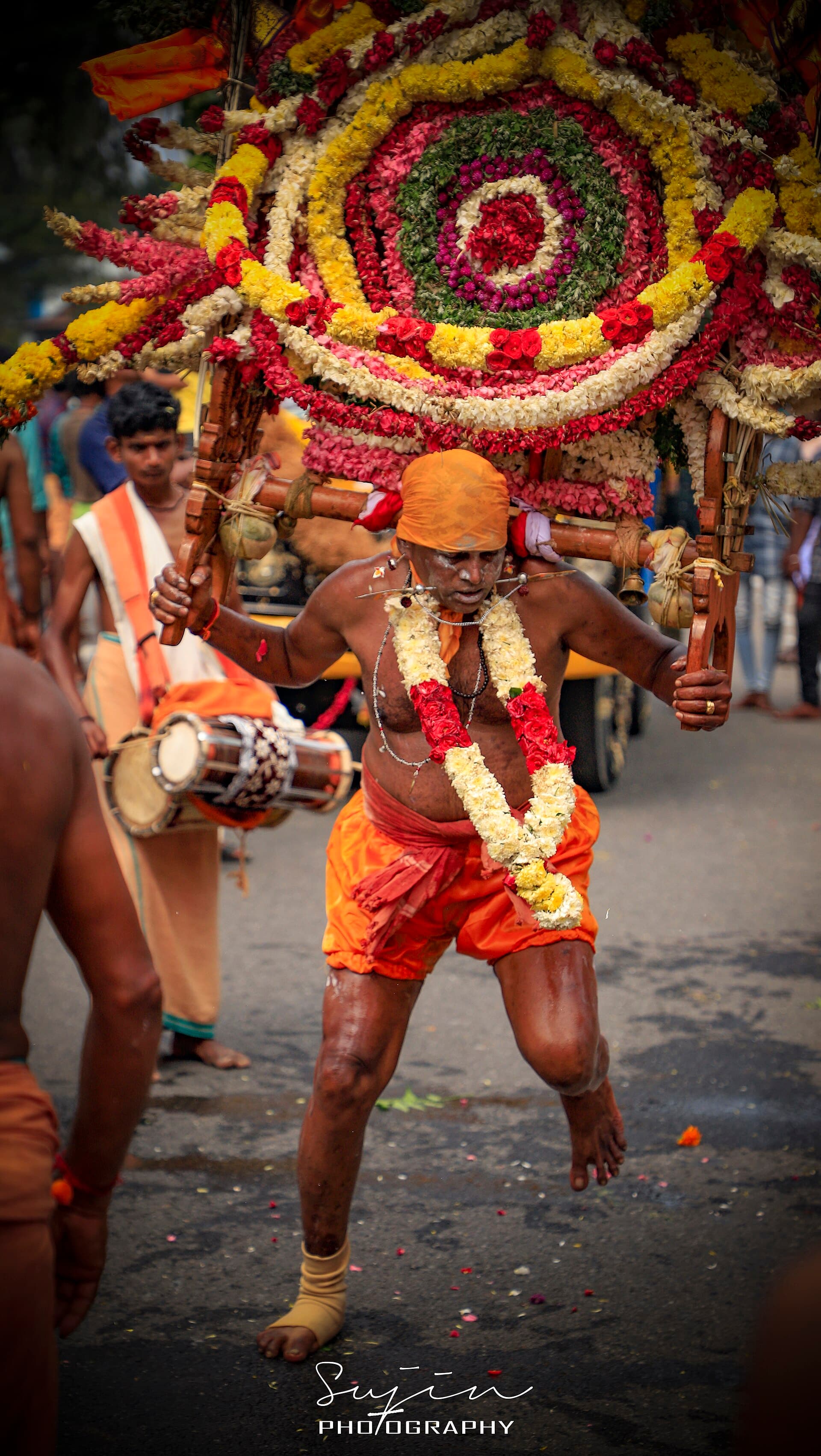 A devotee carrying an ornate peacock-feather kavadi up the Batu Caves steps beside the golden Murugan statue