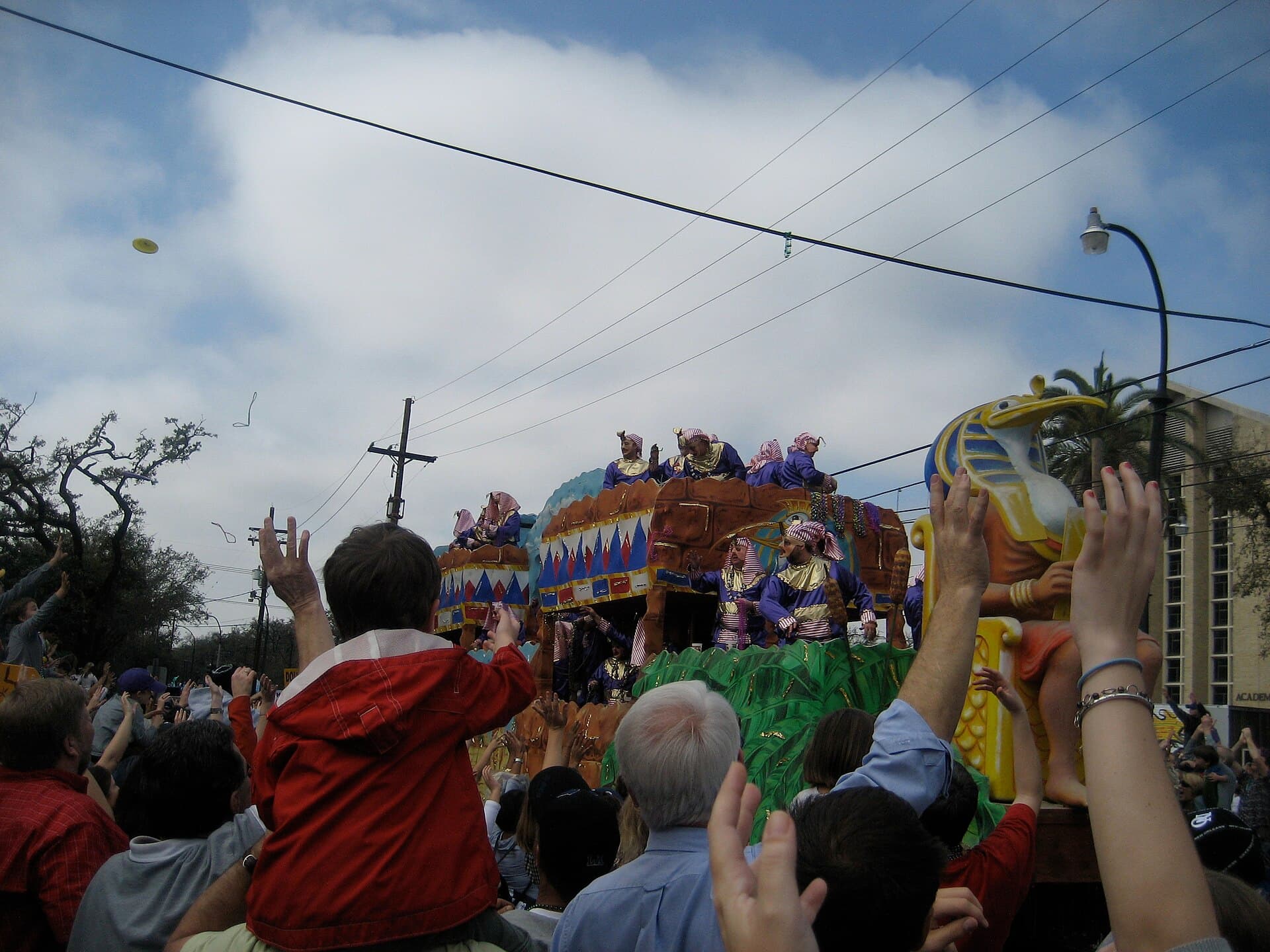 Crowd on the St. Charles Avenue neutral ground reaching up for beads from a passing float under live oak trees