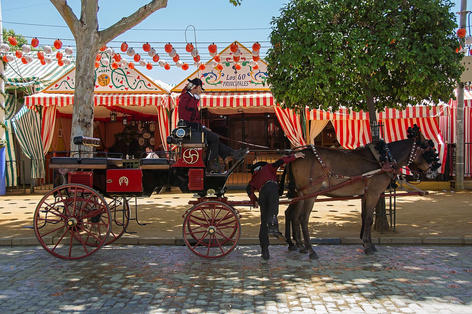 Horse-drawn carriages and riders in traje corto passing along a casetas street at midday