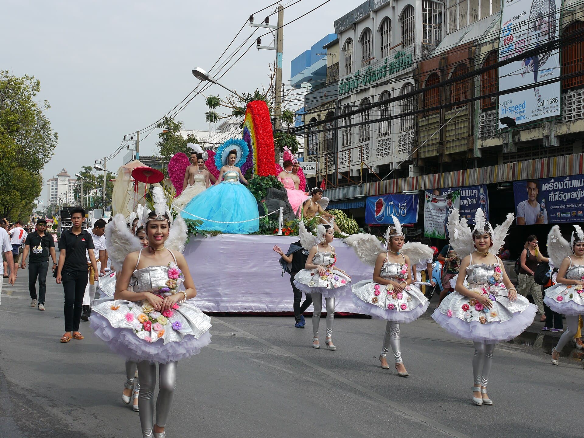 Wide shot of a flower-covered float passing Tha Phae Gate in the Saturday parade, landscape