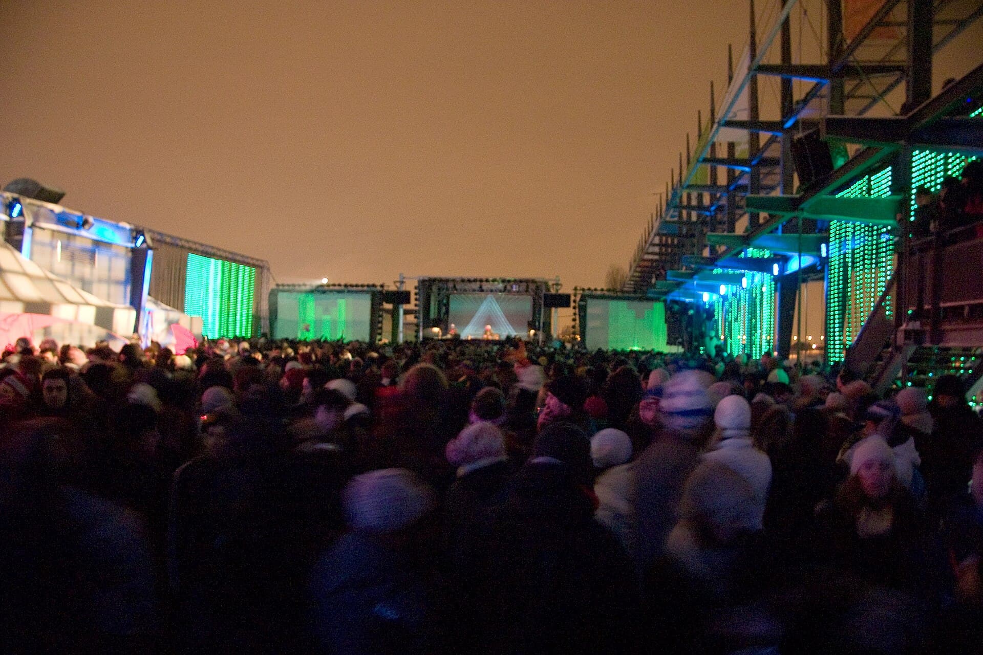 Crowd in parkas and balaclavas dancing outdoors in falling snow at Igloofest