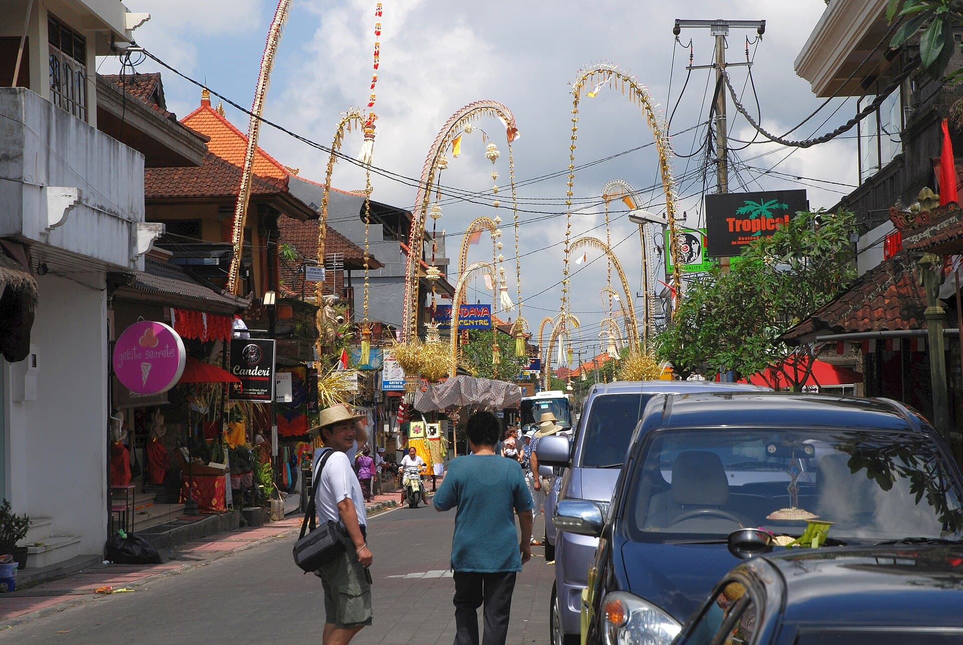 Penjor bamboo poles arching over a village road in Bali during Galungan, wide landscape view