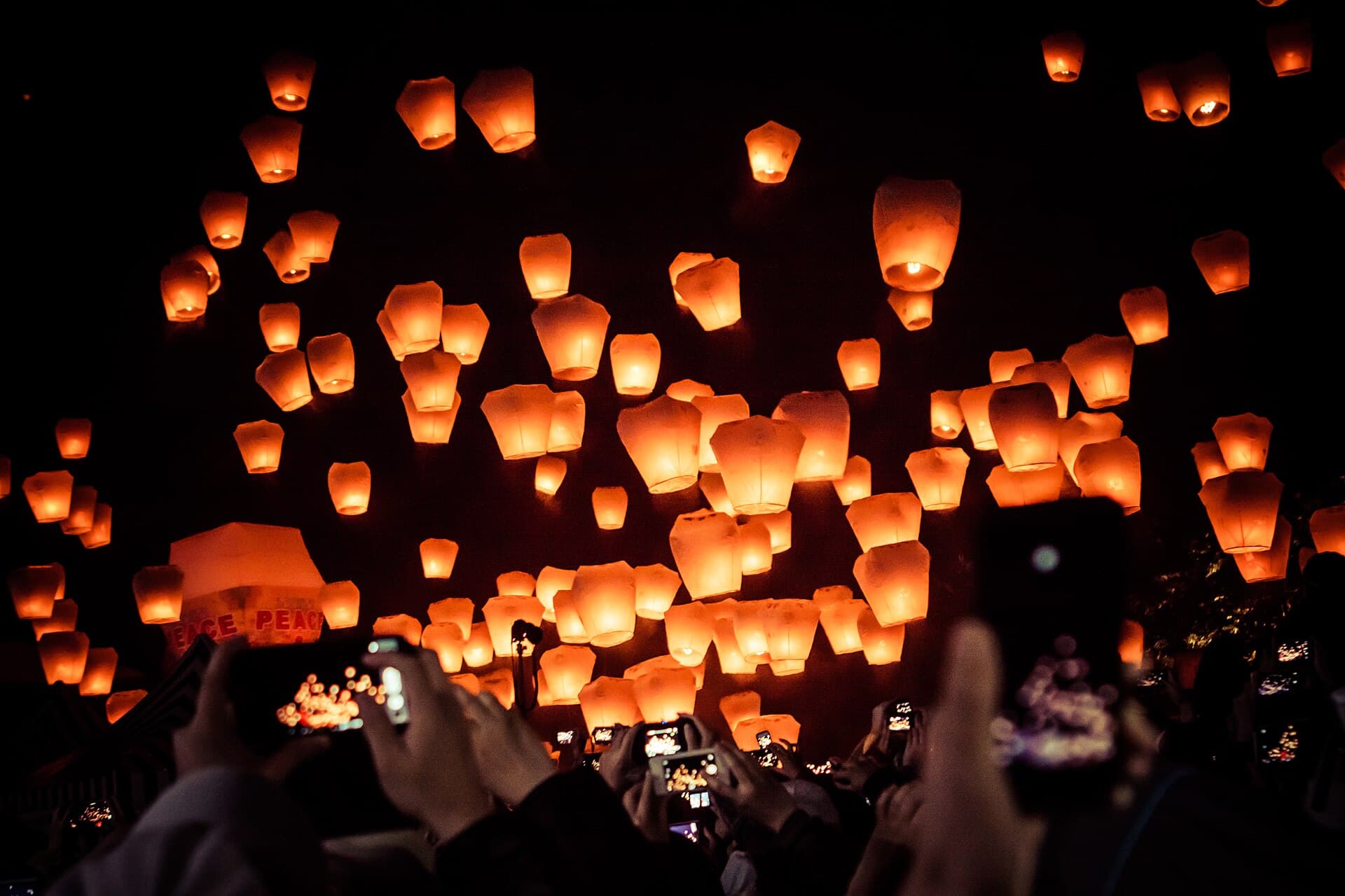 Wide shot of hundreds of glowing sky lanterns rising above the Shifen valley at dusk