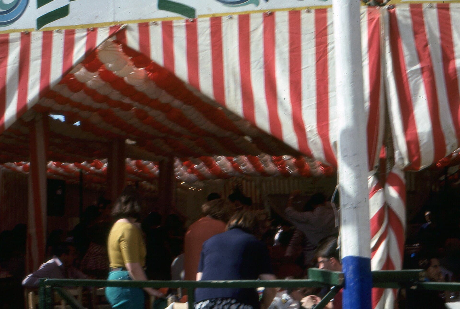 A crowded caseta interior with striped canvas, lanterns, and people dancing sevillanas