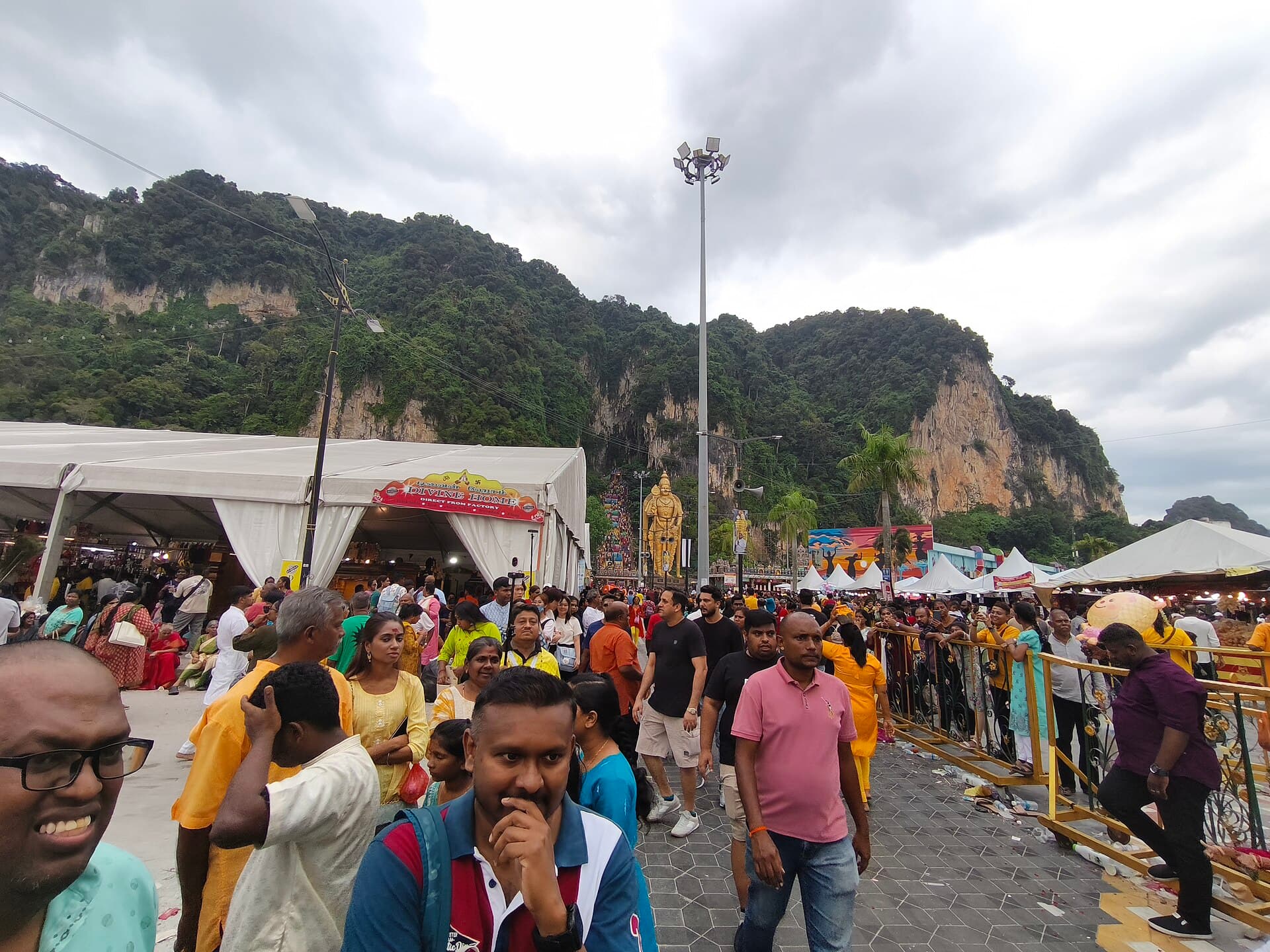 Wide shot of the 272 rainbow-painted steps and the golden Murugan statue at Batu Caves crowded with devotees in yellow