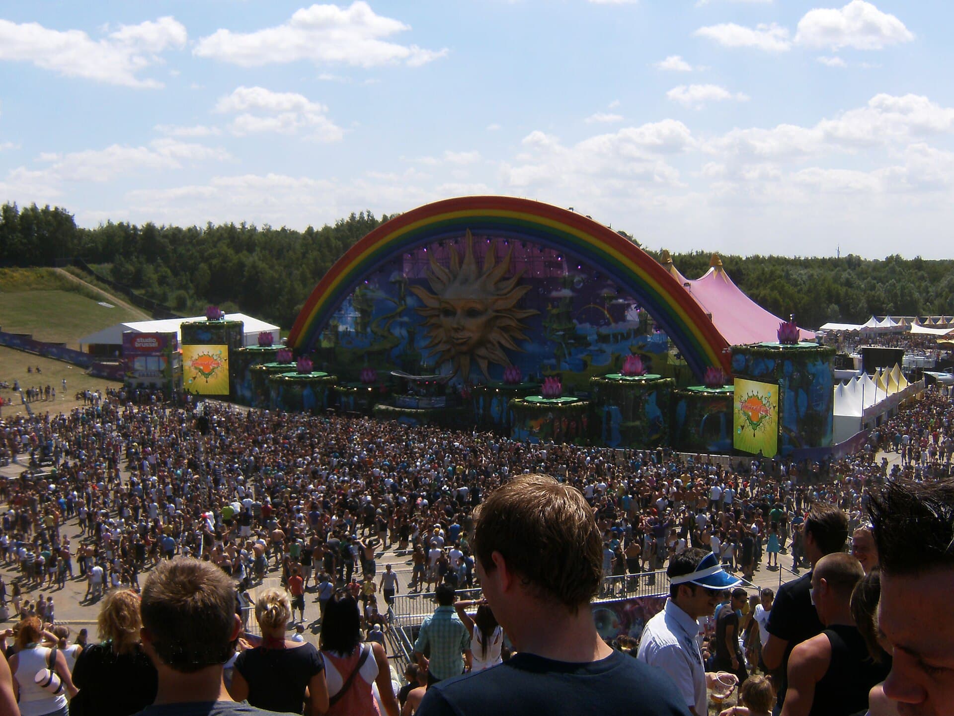 A crowd dancing at a daytime mountain stage in the snow with skiers in the background