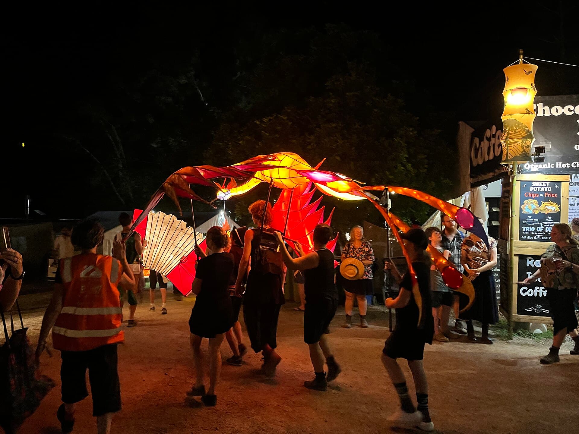 Festival-goers in raincoats and hats walking along a wet path between tents at Woodfordia