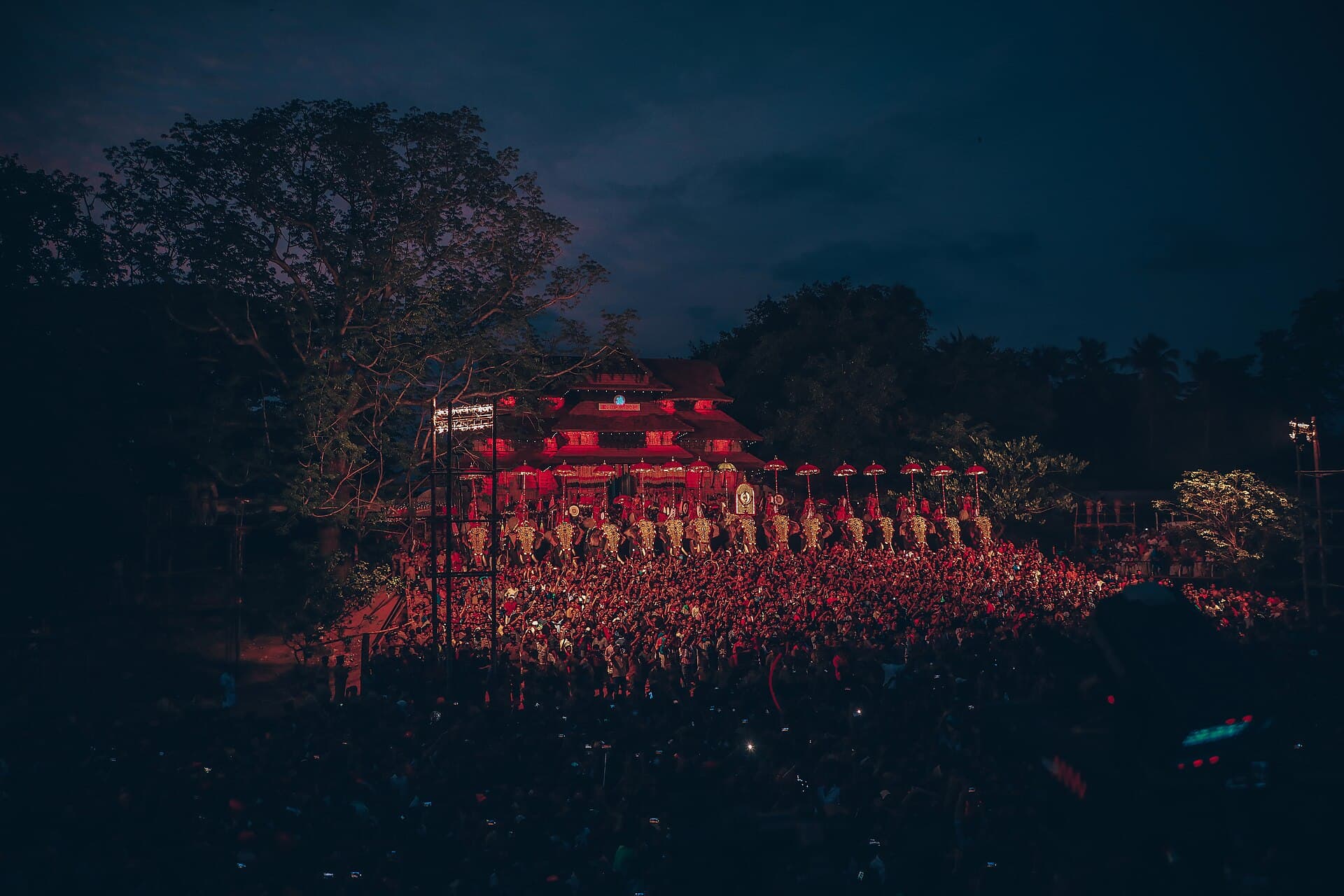 Wide shot of caparisoned elephants lined up for Kudamattam in front of Vadakkunnathan Temple at dusk