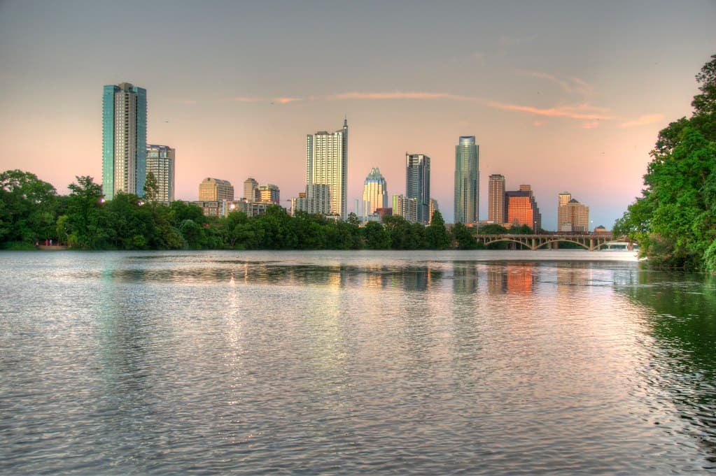 People sitting on the grass at Auditorium Shores on Lady Bird Lake in the spring sun with the downtown Austin skyline behind