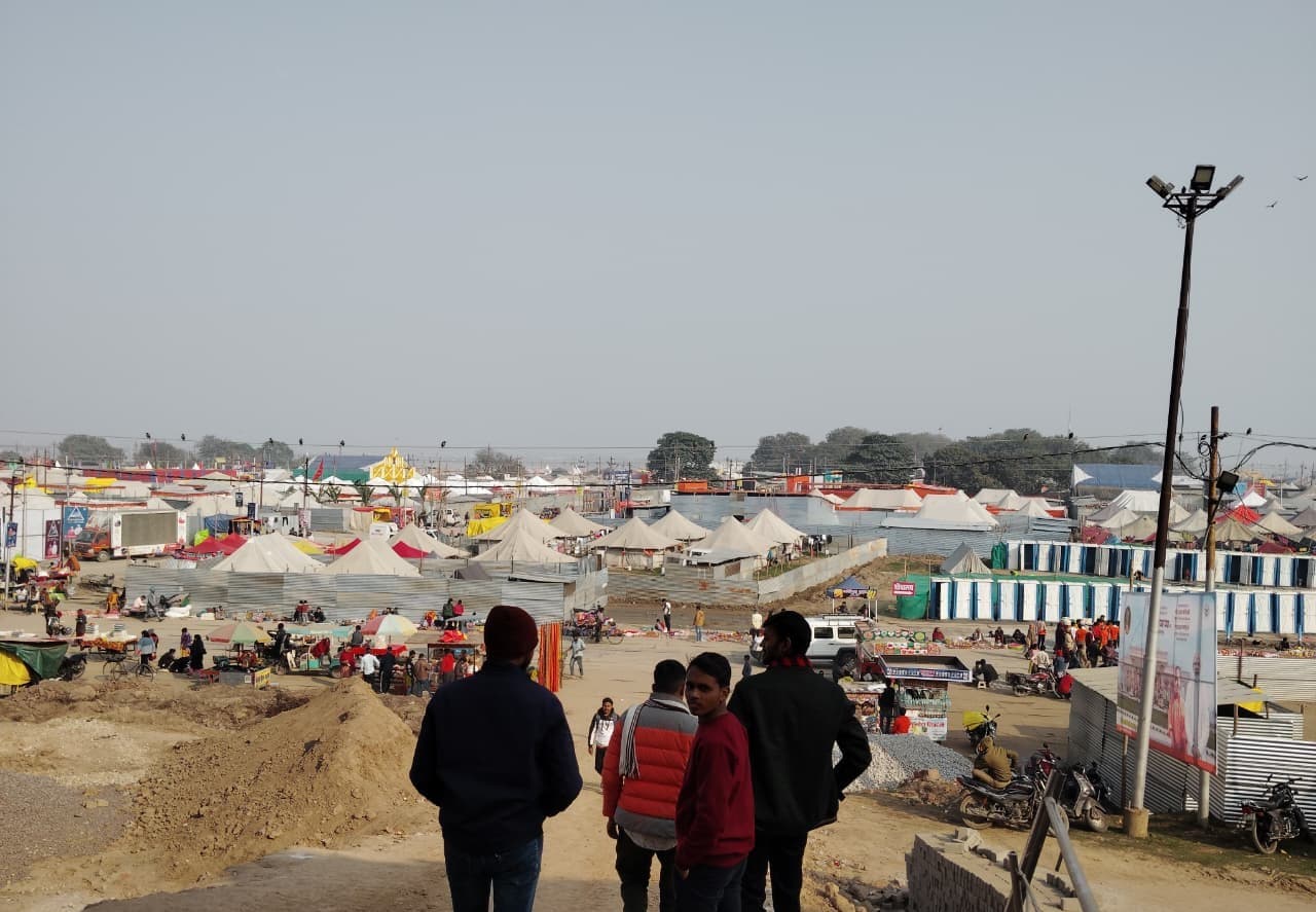 Pilgrims walking along a checkered steel plate road in the Magh Mela ground at Prayagraj