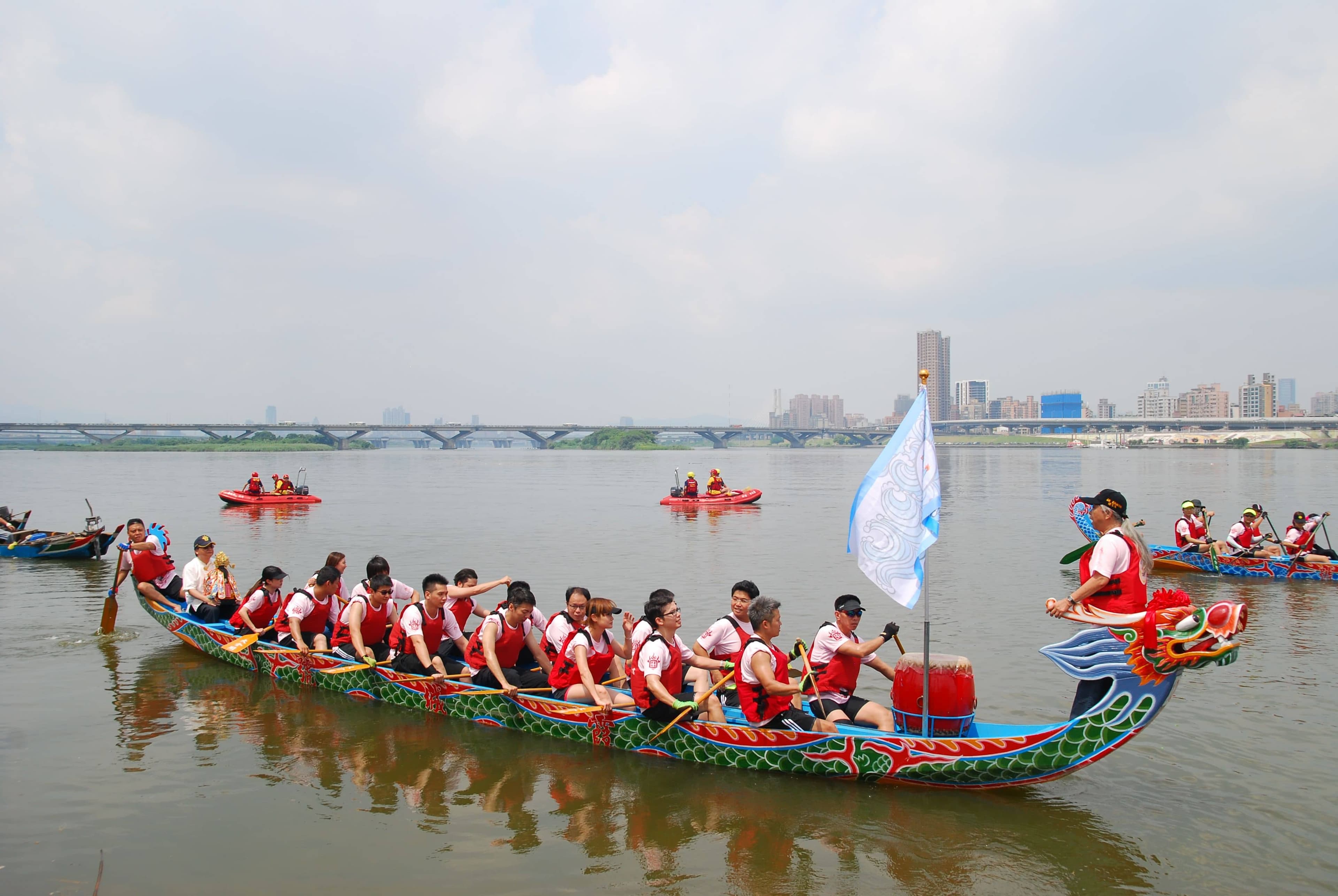 Spectators lining a concrete riverbank railing in Guangzhou watching dragon boats pass, with no ticket barriers in sight