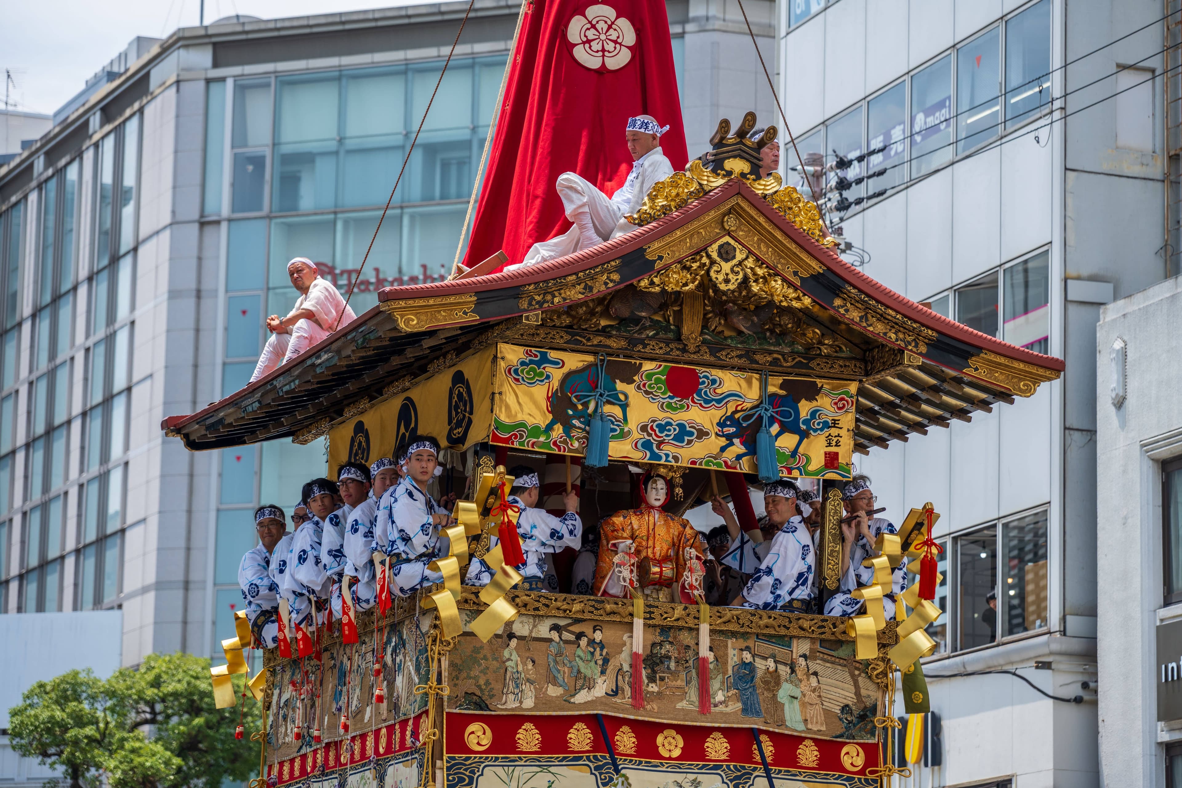 A child in a yukata holding a chimaki charm beside a yamaboko float during Gion Matsuri Yoiyama in Kyoto