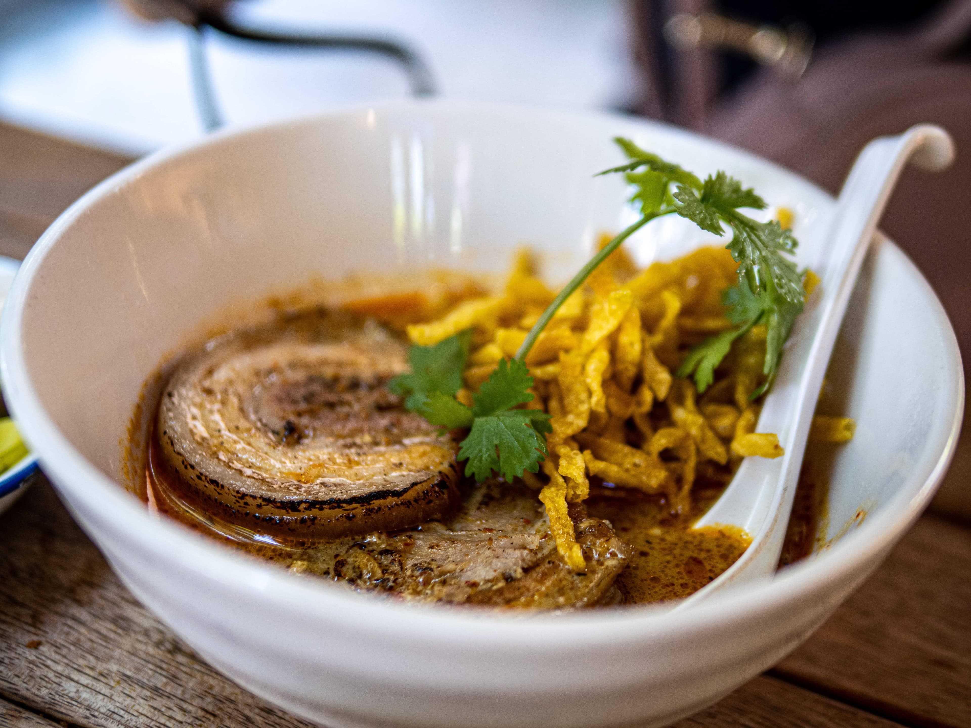 A bowl of khao soi curry noodles with crispy noodles, pickled mustard greens and lime at a Chiang Mai restaurant
