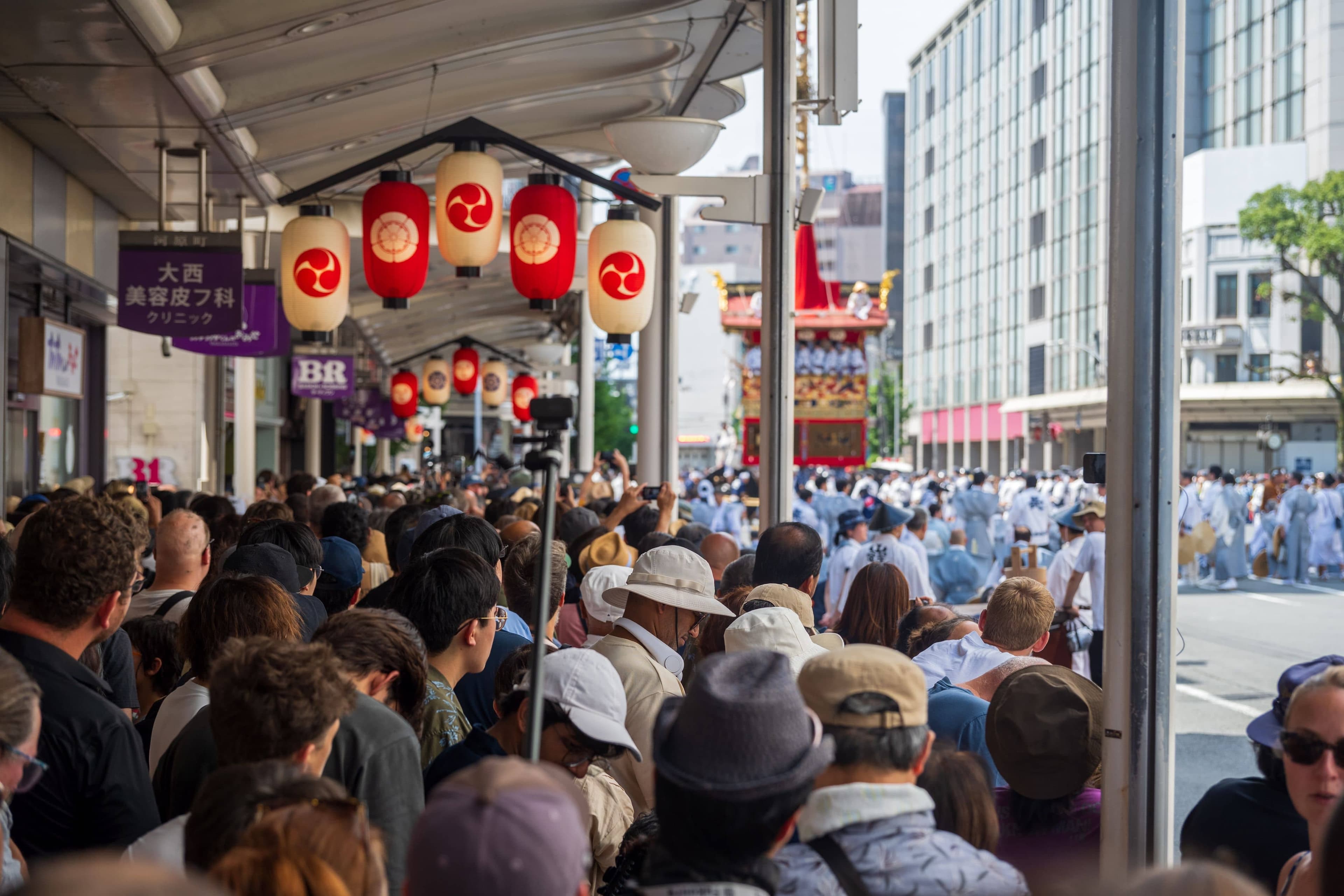 A visitor in a yukata checking a smartphone map in front of a lantern-lit yamaboko float on a crowded Kyoto street at night