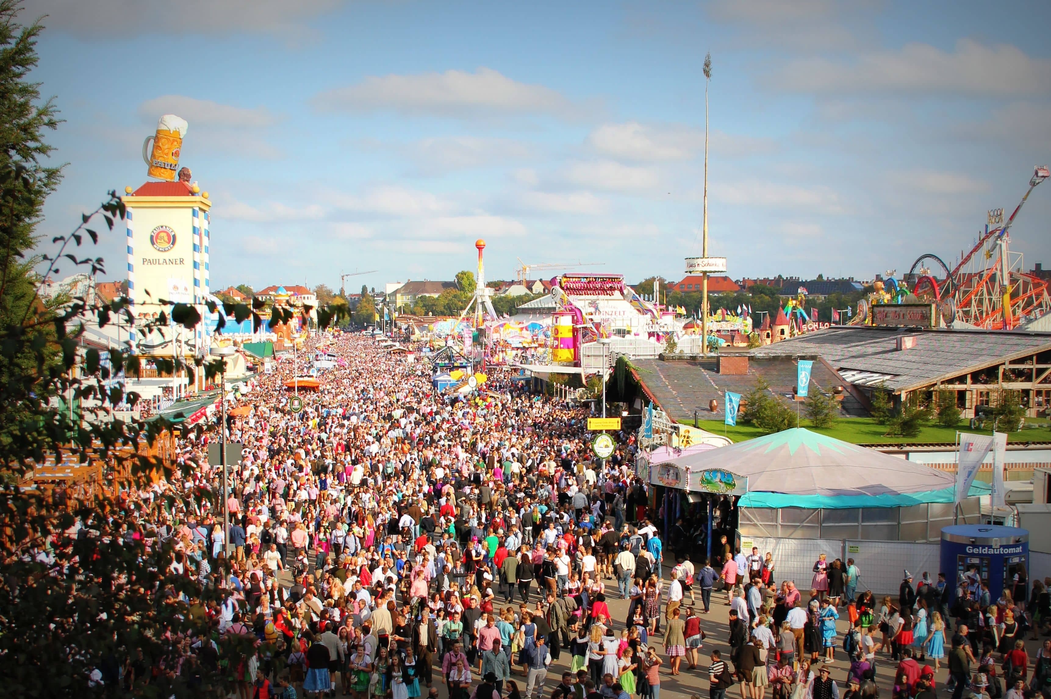 Interior of a packed Oktoberfest beer tent with long tables, a brass band on the central bandstand and servers carrying armfuls of beer steins