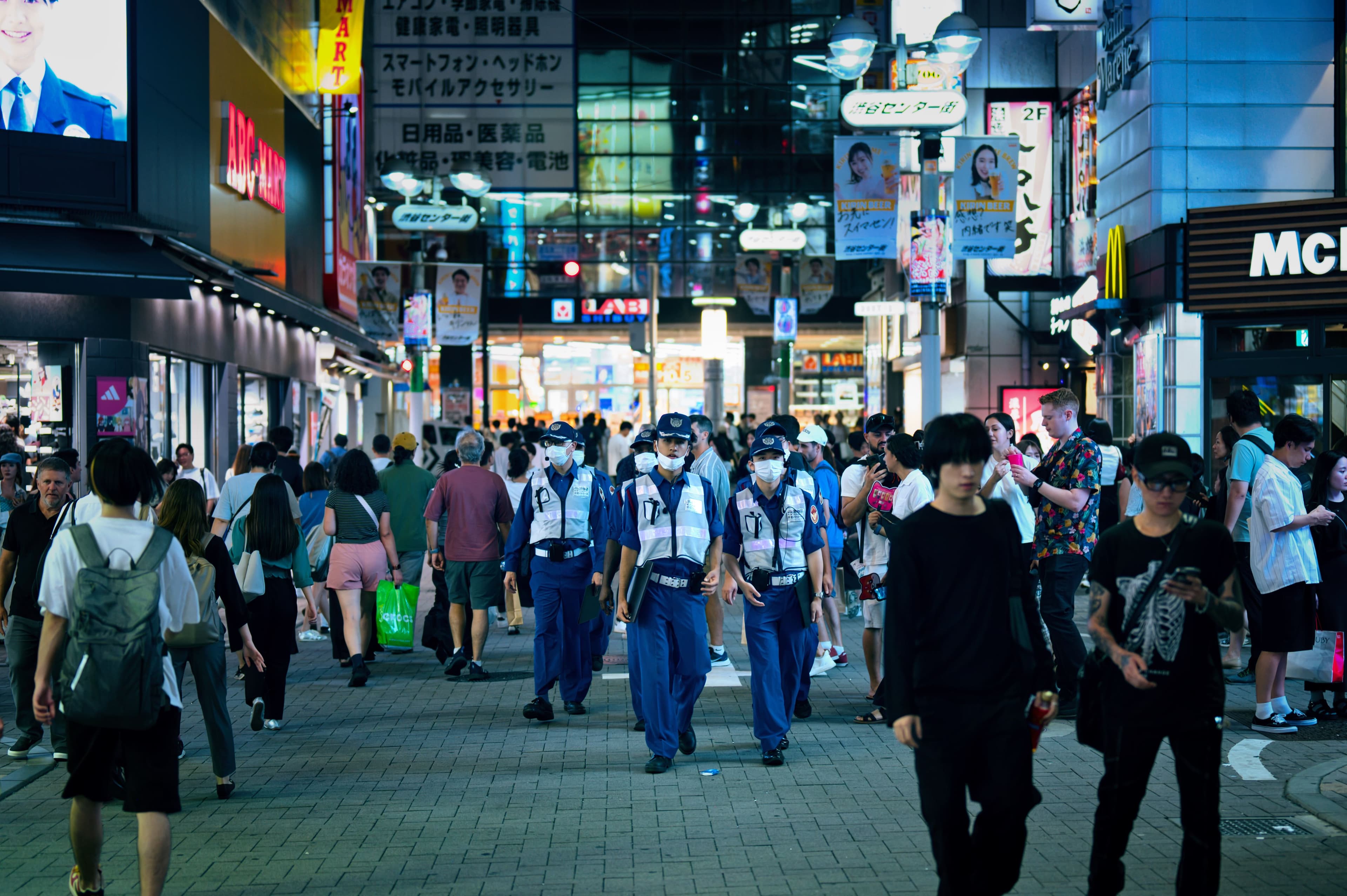 Festival-goers in summer yukata with paper fans and bottled water walking along a sunlit Asakusa street on a hot July afternoon