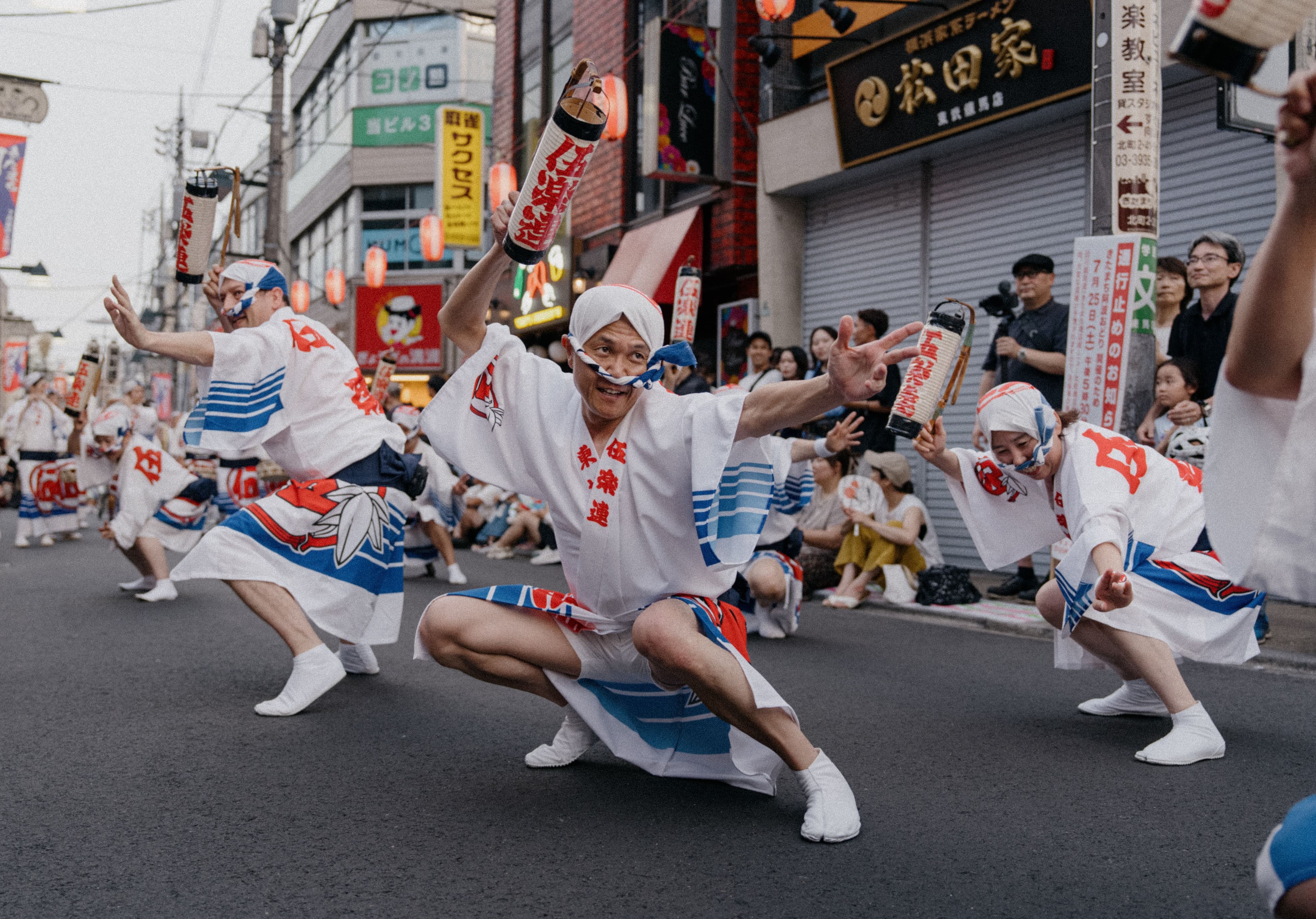 Female Awa Odori dancers in straw amigasa hats and yukata dancing in formation on their geta down a lit Tokushima street