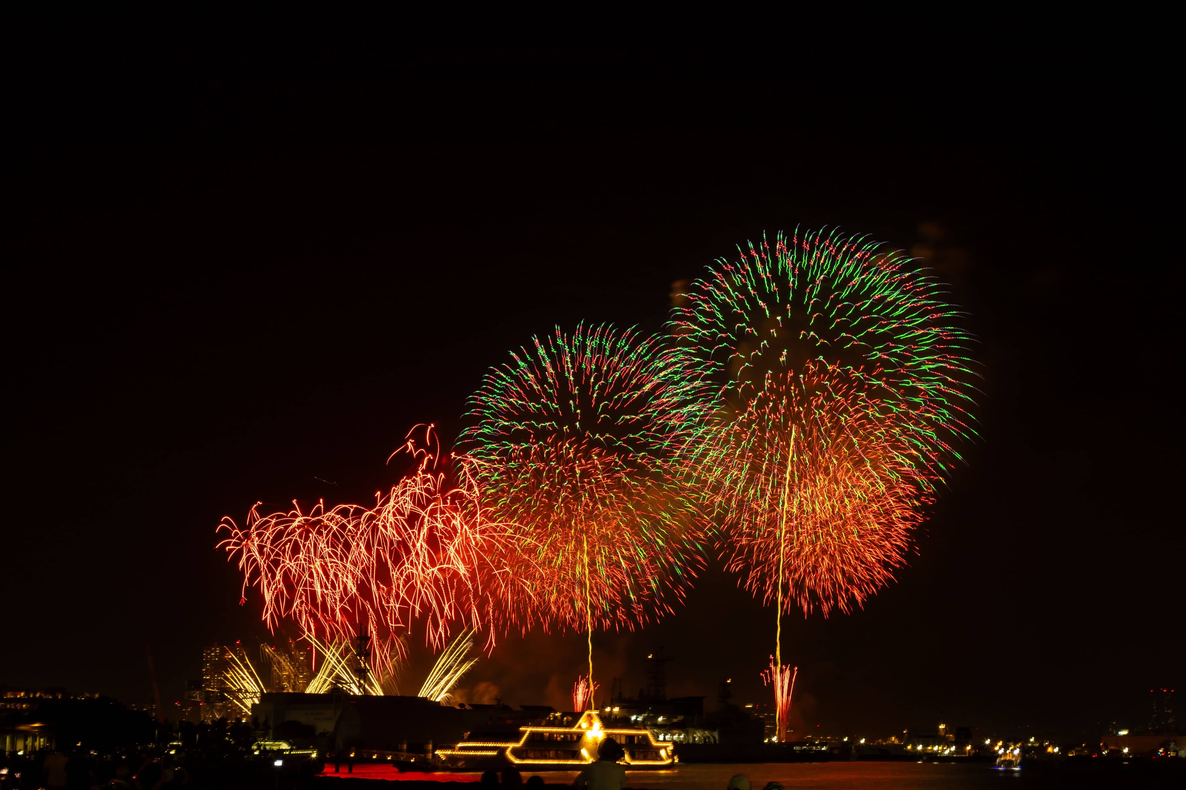 Fireworks bursting over the Sumida River with Tokyo Skytree lit up beside them and the Asahi building in the foreground