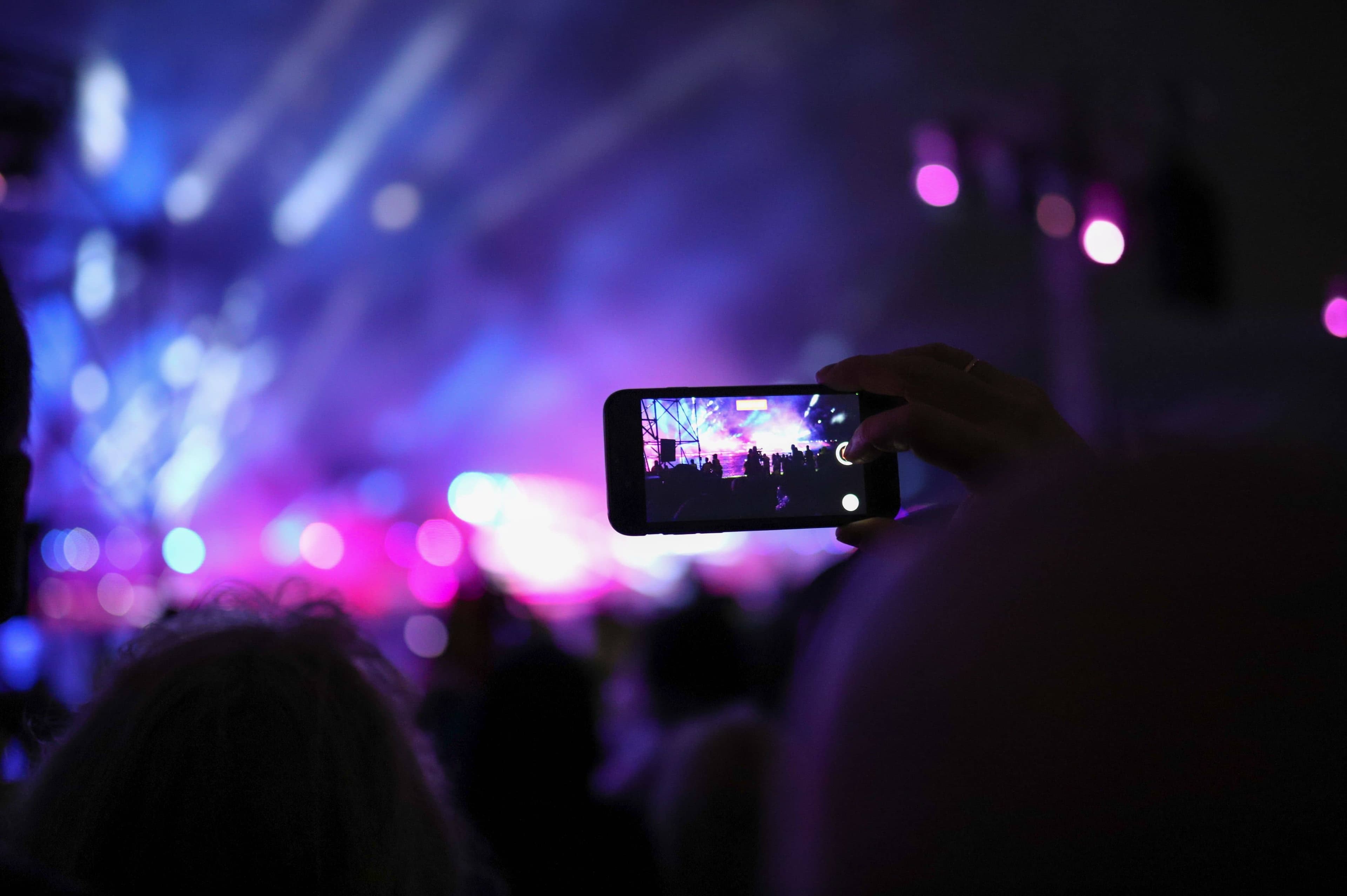 A festival-goer checking a phone timetable app in front of a stage at Fuji Rock Festival with trees and string lights around