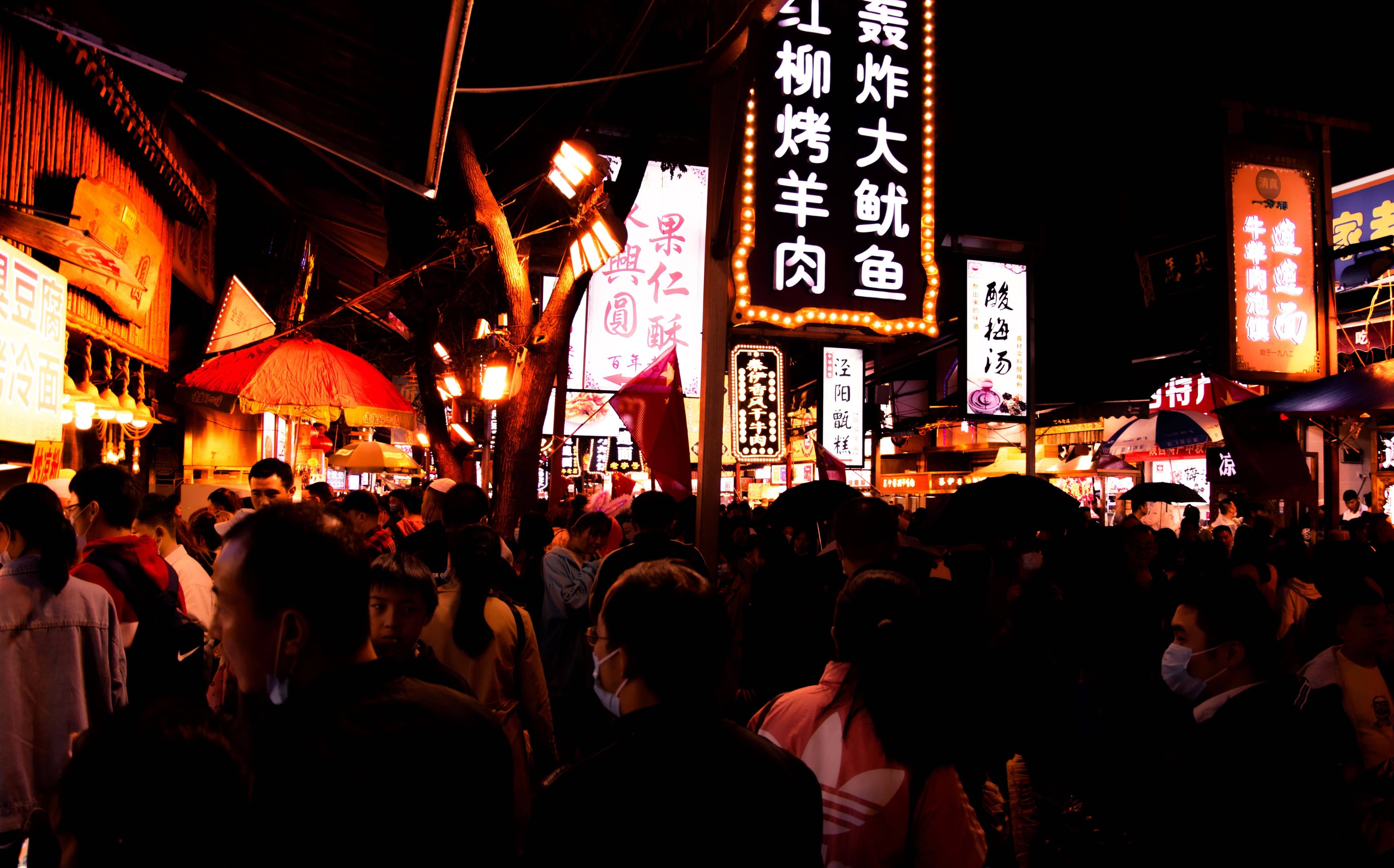 Visitors in winter coats and scarves walking under rows of red lanterns on a cold, clear evening in Shanghai's Old City